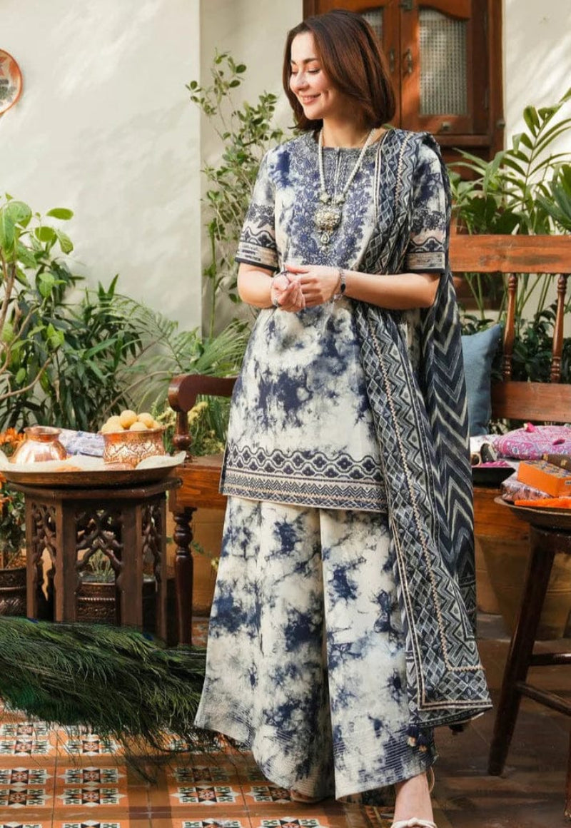 Woman in a blue and white patterned outfit standing in a room with plants and furniture.